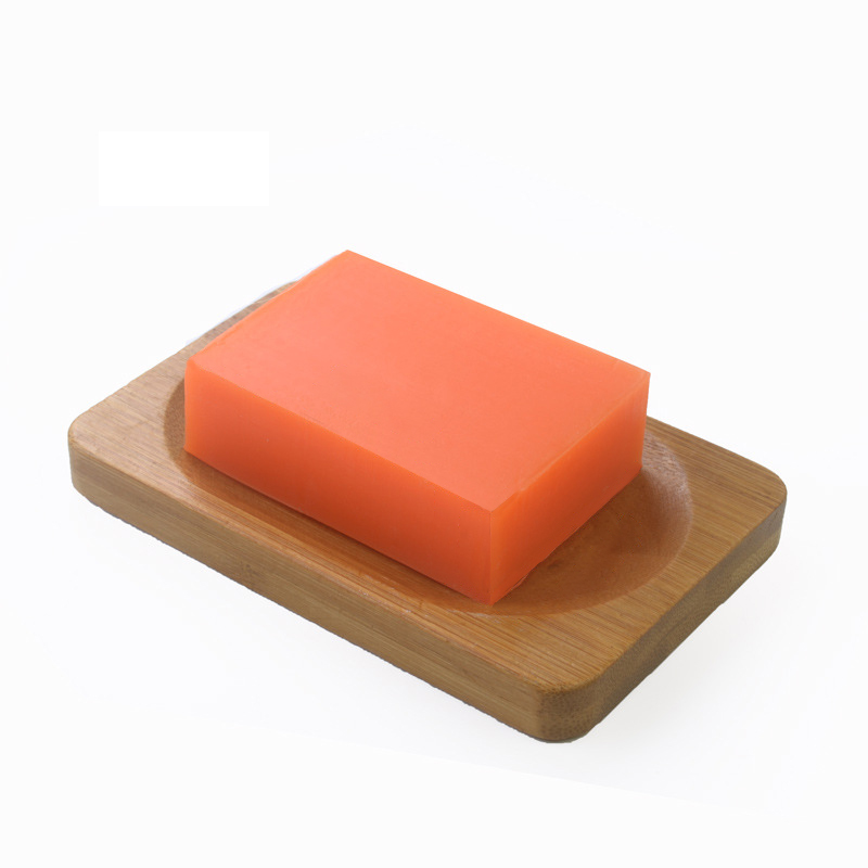 Kojic Acid - Bright orange bar of soap on a wooden soap dish, set against a clean white background. The scene is simple and fresh, evoking cleanliness.