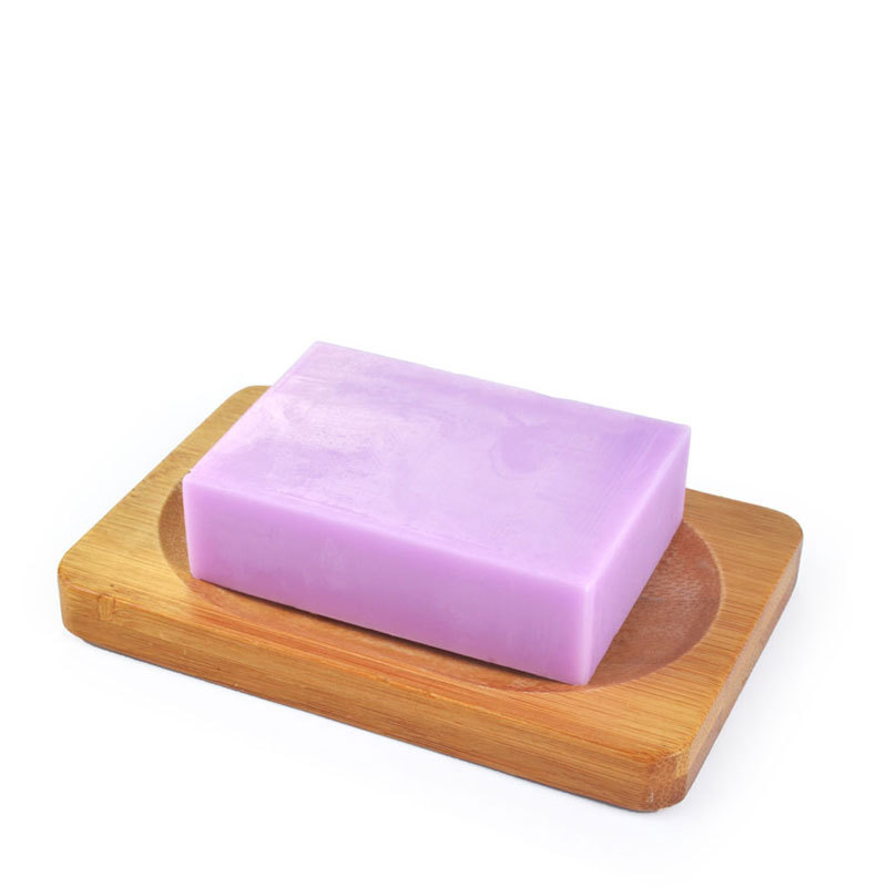 A lavender soap bar rests on a smooth, wooden soap dish with an indented center. The scene is clean and conveys a sense of freshness.