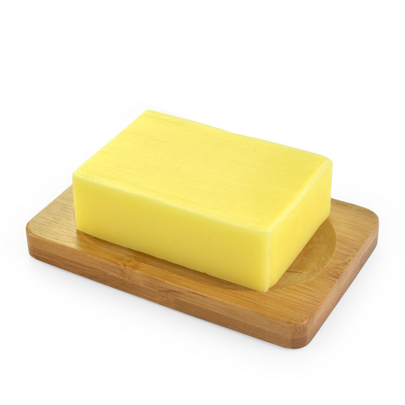 A rectangular block of butter resting on a wooden butter dish against a white background.